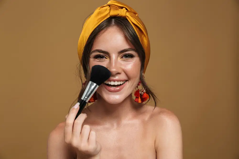 Imagem de mulher sorrindo e segurando um pincel para blush próximo ao rosto