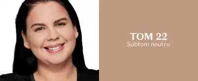 Mulher de pele branca e cabelos pretos está sorrindo para a câmera em fundo branco e, ao lado, em fundo bege, letras brancas indicam que o tom de pele dela é 22, com subtom neutro.