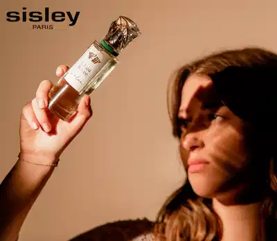 Uma mulher segurando um frasco de perfume Sisley, com o logotipo da marca visível na imagem.