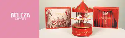 O banner apresenta  coleção de produtos da marca Beleza Express, incluindo uma caixa com ilustração de um circo, um carrossel vermelho e um livro.