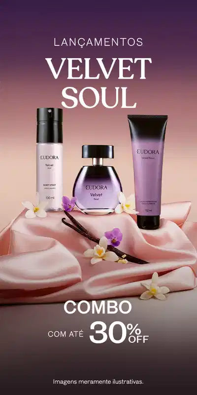 Três frascos da linha Velvet Soul Eudora: um Desodorante Colônia, um Body Spray e uma Loção Corporal. Os produtos estão dispostos sobre uma superfície rosa, com flores brancas e violetas ao redor.