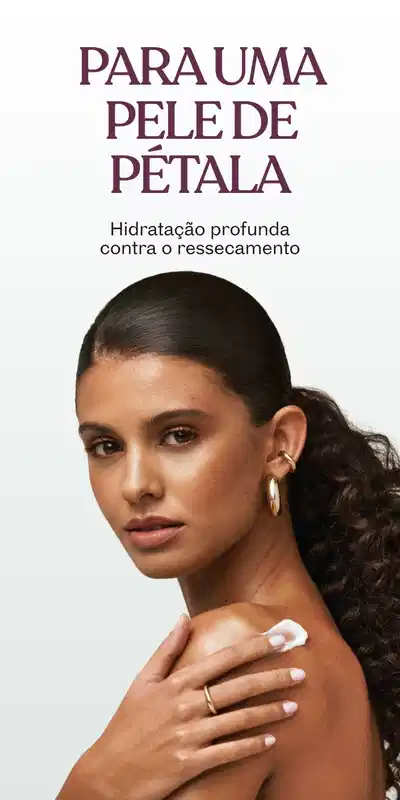 Mulher com cabelos presos atrás da orelha, aplicando creme corporal no ombro, comunicando hidratação profunda como o ressecamento.