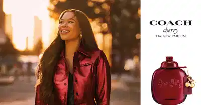 A imagem mostra o novo Coach Cherry Parfum, perfume de frasco vermelho com a tradicional carruagem Coach estampada na frente.