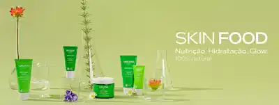 Linha Skin Food Weleda com fundo verde claro. Diversos produtos em tubos e potes verdes com rótulos Weleda Skin Food, acompanhados de flores naturais como rosa laranja, flor roxa e margarida branca, além de garrafas de vidro transparente. Texto em branco à direita: "SKIN FOOD Nutrição. Hidratação. Glow. 100% natural".