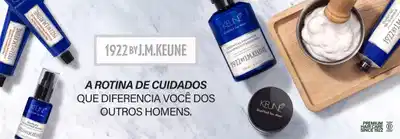 Composição de produtos da linha 1922 by J.M. Keune para homens sobre superfície de mármore. À esquerda, frascos azuis e pretos contendo shampoo e produtos capilares. No centro, frasco azul escuro com shampoo essencial de 250ml. À direita, pote de madeira com creme branco e frascos adicionais. Logo "1922 by J.M. Keune" centralizado no topo. Texto em destaque: "A Rotina de Cuidados que Diferencia Você dos Outros Homens". Selo "Premium Hair Care Since 1922" no canto inferior direito. Marca "Keune Distilled for Men" visível em produtos.