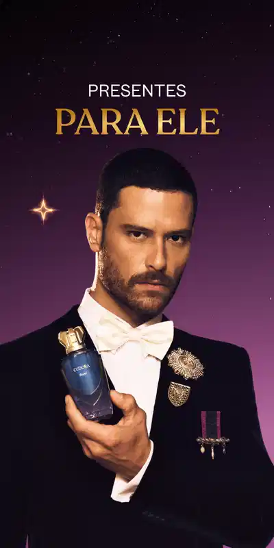 Presentes para ele, homem de terno preto e gravata borboleta branca segurando frasco de Eau de Parfum Eudora Royal, em fundo com tons de roxo e efeitos de luz dourada.