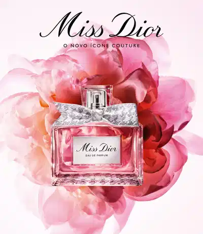 A imagem apresenta uma composição de flores rosas e brancas, com um frasco de perfume da marca Miss Dior no centro. O frasco possui um laço prateado e a embalagem exibe o nome da fragrância em destaque.