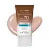 Frasco de 40ml de protetor solar facial com cor 1.0 FPS 70 Boti.Sun em embalagem marrom e branca e rótulo com letras brancas contendo informações sobre o produto. Ele está à frente de uma quantidade do produto mostrando textura e tonalidade bege claro.