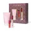 O conjunto de produtos Eudora apresentado inclui uma loção hidratante corporal, uma máscara para cílios e um gloss labial da linha Niina Secrets de Eudora. Junto, temos uma embalagem composta por uma caixa com padrões geométricos em tons de roxo e dourado