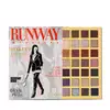 A paleta de sombras Eudora com 24 tons em embalagem retangular dourada, acompanhada de uma revista de moda "Runway" com ilustração de uma mulher de terno preto.