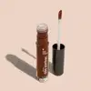 Frasco cilíndrico transparente contendo um gloss labial marrom. Rótulo na embalagem com o nome do produto "Gloss dos Sonhos" e a descrição "Quem disse, berence?". Ao lado, a tampa preta do produto, que acompanha um aplicador de espuma.