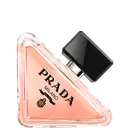 Frasco de perfume Prada com design triangular em vidro transparente, contendo líquido de cor rosa clara. O rótulo preto destaca o nome da marca "PRADA" em letras brancas.