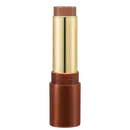 Bronzer em Bastão em embalagem cilíndrica. O estojo é de metal dourado com detalhes em tom de marrom. A parte superior e inferior são de cor cobre fosco. A embalagem tem um design elegante e sofisticado.
