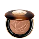 A imagem mostra o sérum iluminador Lancôme. A embalagem é redonda com tampa marrom e logotipo dourado no centro. A parte inferior preta com aro dourado. Interior contém o pó iluminador marrom com padrão rendado.