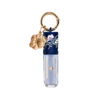 Embalagem de gloss labial da marca Bruna Tavares com textura suave e brilho, na cor Diamond, acompanhada de pingente dourado em formato de flor.
