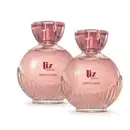 Dois frascos de item de perfumaria da marca Liz Sublime, com embalagem de vidro arredondada rosa-claro facetado e nome da marca em vermelho escuro gravado no vidro. A tampa é em acrílico transparente e permite ver a tampa borrifadora de tom metálico rosa.