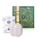 Imagem de dois sabonetes brancos com a marca Cuide-se Bem gravada no produto e sua caixa branca que traz ilustração de flores azuis com a linha Rosa e Algodão em letras pretas, além de uma caixa presenteável verde com fita e estampa douradas.

