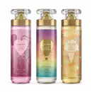 Imagem de três frascos de body splash Dream: um com rótulo roxo da linha Amor no Ar, um com rótulo colorido da linha Viagem Encantada e outro com rótulo dourado da linha Céu de Baunilha. As embalagens são de vidro com válvula spray dourada.