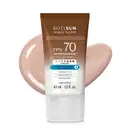 Frasco de 40ml de protetor solar facial com cor 1.0 FPS 70 Boti.Sun em embalagem marrom e branca e rótulo com letras brancas contendo informações sobre o produto. Ele está à frente de uma quantidade do produto mostrando textura e tonalidade bege claro.
