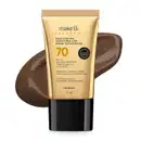 Bisnaga de base líquida protetora com ácido hialurônico da marca Make B., com FPS 70, embalagem em tubo dourado e tampa preta, com informações sobre benefícios e tecnologia prebiótica impressas. Ao fundo, um splash de base na cor marrom escuro.
