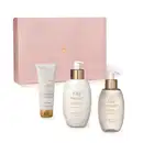Caixa rosa com detalhe dourado e três produtos de cuidados corporais da marca Lily: bisnaga de creme acetinado corporal, frasco de creme de banho acetinado e outro frasco de sabonete líquido, todos em tons de dourado e branco.