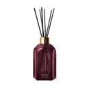 Frasco de difusor de aromas da marca Casa 214, com design geométrico em vidro de cor roxa escura e tampa dourada. Contém varetas de difusão pretas inseridas no frasco.
