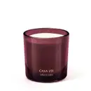 Vela aromática em recipiente de vidro de cor vinho com rótulo "Casa 214 o Boticario" em letras douradas. O recipiente possui formato cilíndrico e a vela em seu interior parece ser de cor clara.
