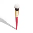 A imagem mostra um pincel de maquiagem, visto de um ângulo um pouco mais elevado, sem ser exatamente de frente. Com cabo vermelho e dourado, e cerdas pretas com ponta branca. Na parte vermelha, logo da marca e linha do produto escrito em dourado.