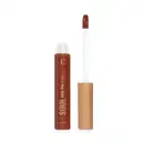 Frasco de vidro transparente contendo gloss marrom caramelo achocolatado. Rótulo com o nome do produto e da marca em letras douradas sobre fundo transparente do frasco e marrom do produto. Aplicador de espuma em formato de pincel firme. Tampa dourada