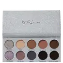 Paleta de sombras de olhos compacta com embalagem retangular de aparência glitter prateada. A caixa contém 10 sombras prensadas em tons neutros e profundos, variando do bege claro ao marrom escuro.