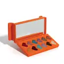 Paleta de sombras em formato de caixa laranja com espelho, contendo 12 sombras em formato de coração em tons de marrom, roxo, azul e dourado.