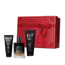 Conjunto. No centro, frasco de vidro contendo líquido da fragrância em degradê de preto à âmbar, de alto a baixo. Ao lado, tubo preto de gel de banho e um tubo preto de creme de barbear. Acompanha caixa vermelha com detalhes em dourado e laço vermelho.