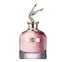 Perfume em frasco de vidro rosa com tampa metálica dourada em forma de pernas femininas. O frasco tem base cromada e o rótulo exibe o texto "SCANDAL" em letras maiúsculas douradas.
