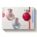 Três vidros redondos com florais em relevo, borrifador dourado e tampa cristal de desodorante colônia Floratta, sendo um rosa transparente da linha Rose, um azul transparente da linha Blue e um vermelho da linha Red, acompanhados de uma caixa de presente.