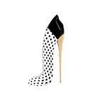 Frasco do perfume Good Girl Blush Polka Paradise em forma de sapato de salto alto com estampa de bolinhas pretas e brancas, com detalhes em dourado na parte superior e no salto. Embalagem elegante e minimalista, em preto e branco.