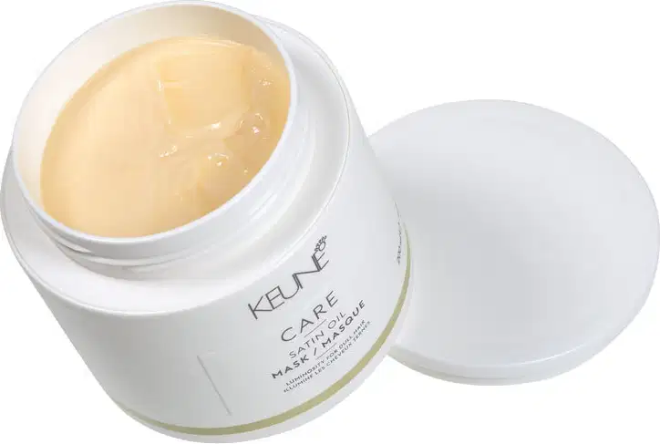 Recipiente branco de creme hidratante da marca Keune, com textura cremosa e brilhante, em um ambiente limpo e minimalista, sugerindo um produto de cuidados com a pele.