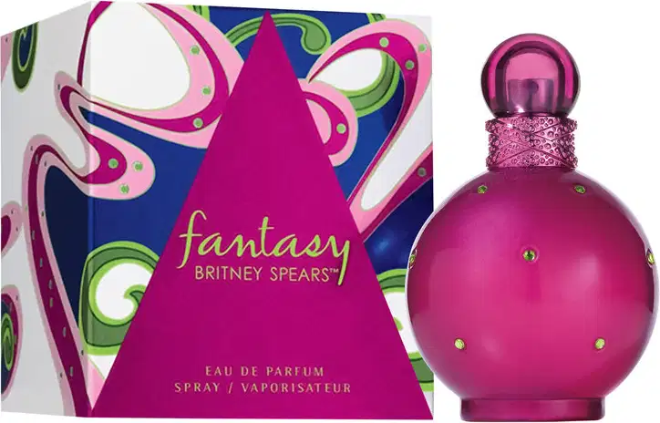 Perfume Fantasy da marca Britney Spears. Frasco de vidro arredondado na cor rosa vibrante com detalhes de strass. Caixa retangular com design abstrato em tons de rosa, azul e verde, exibindo o nome "Fantasy" e a marca Britney Spears em letras douradas.