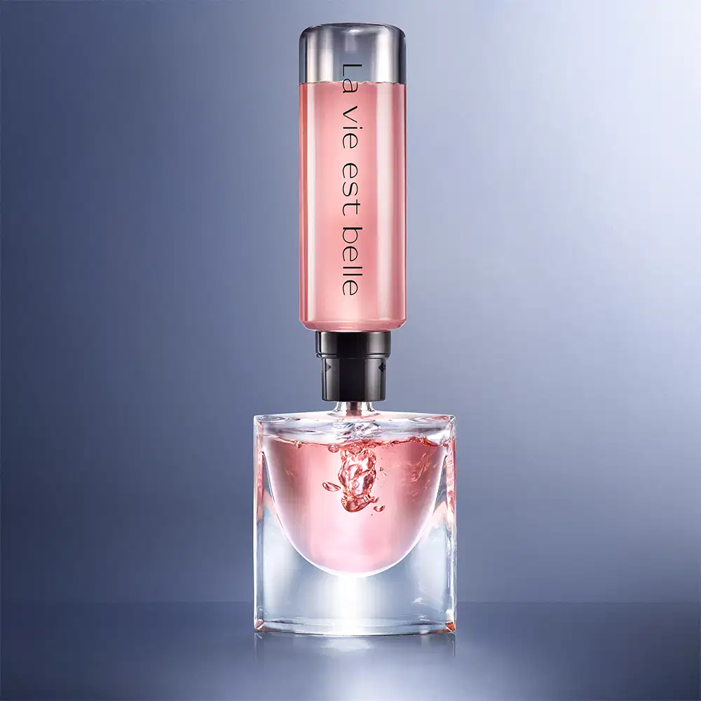 Frasco de perfume Lancôme com tampa prateada e rótulo rosa, contendo líquido rosa claro. Embalagem de vidro transparente com design elegante e sofisticado.