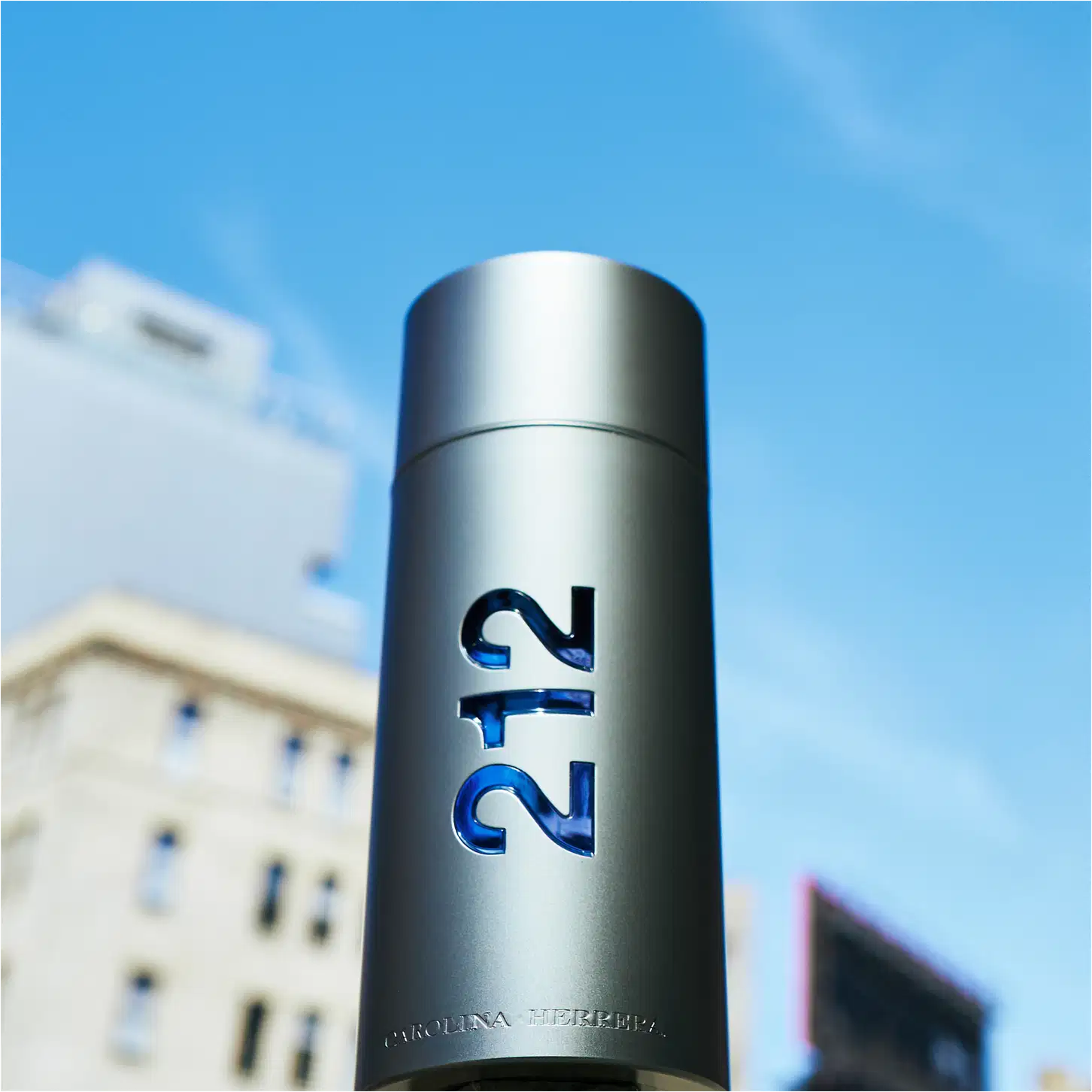 Frasco de perfume Carolina Herrera 212, com design cilíndrico prateado e números azuis "212" impressos. Embalagem elegante e minimalista, refletindo a sofisticação da marca.