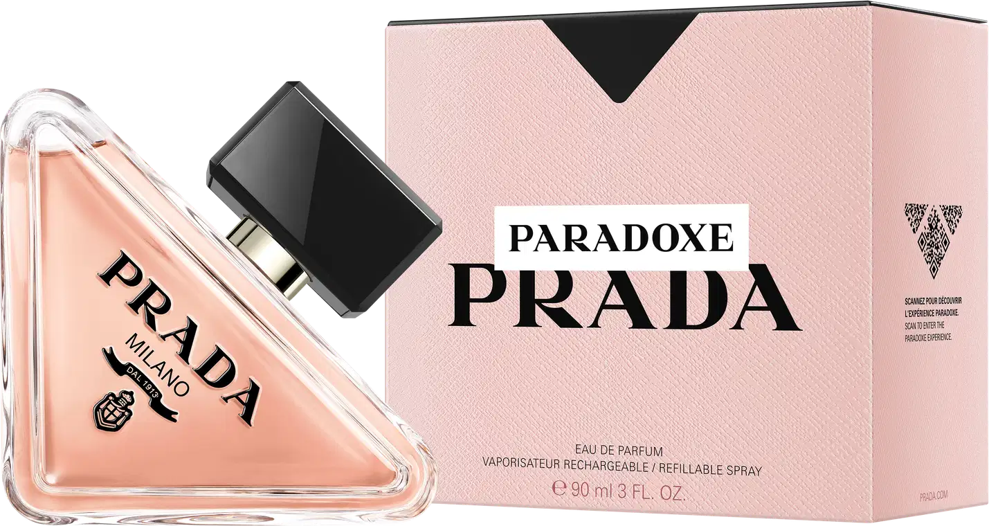 Frasco de perfume Prada com design triangular em vidro transparente, contendo líquido de cor rosa clara. O rótulo preto destaca o nome da marca "PRADA" em letras brancas.