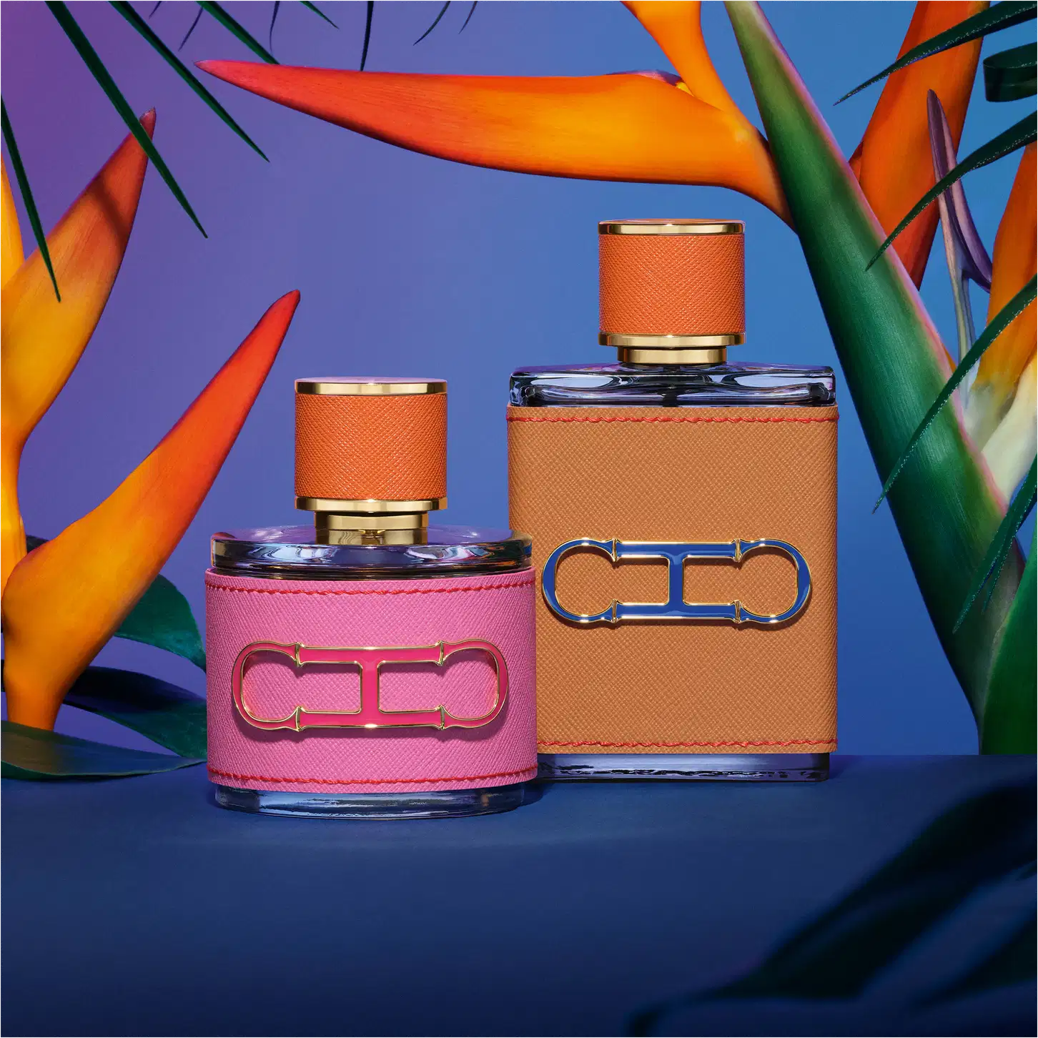 A imagem mostra dois frascos de perfumes, da mesma coleção. Um menor, arredondado, com capa rosa e tampa laranja, e um maior, retangular, com capa e tampa laranja. Ambos apresentam a logo da marca em alto relevo.