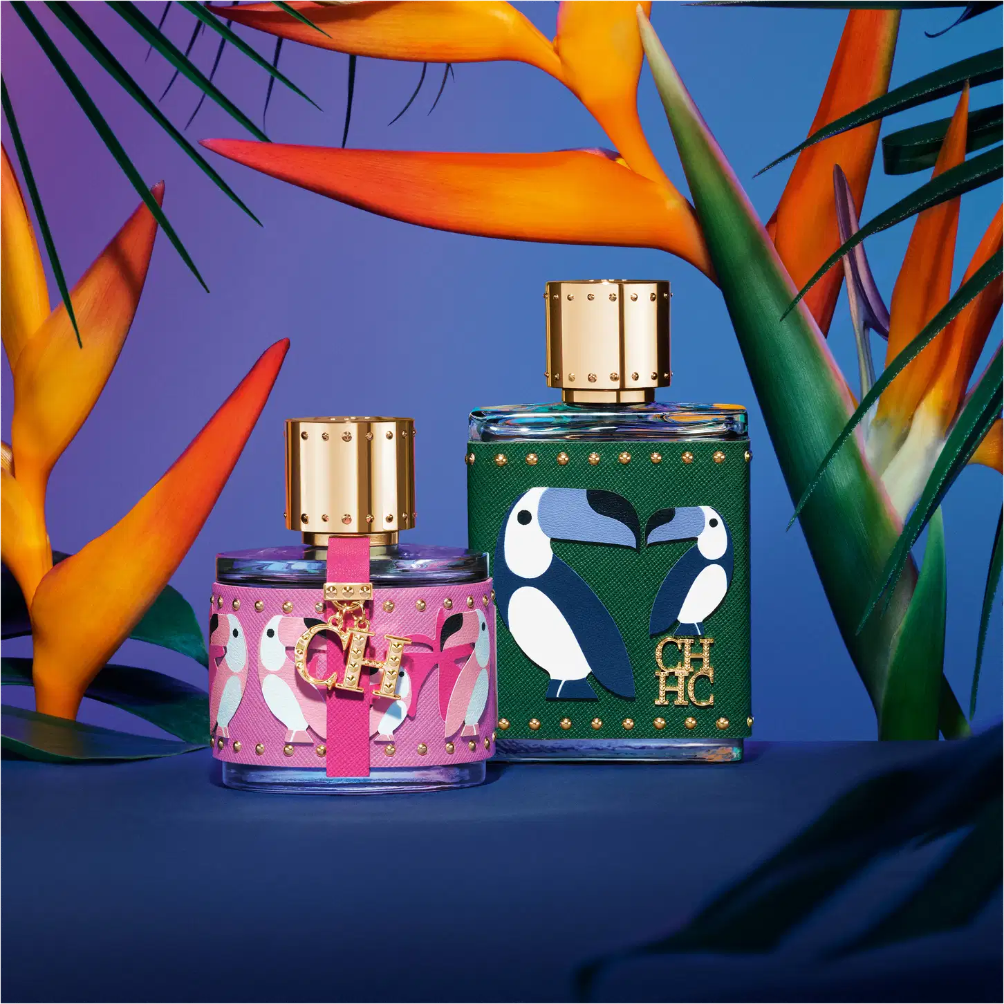 A imagem mostra dois frascos de perfume da marca Carolina Herrera, do lado esquerdo, um frasco pequeno, arredondado, com capa rosa com estampas de pássaros rosa e detalhes dourados. Do lado direito, o frasco de CH Men Birds of Paradise.