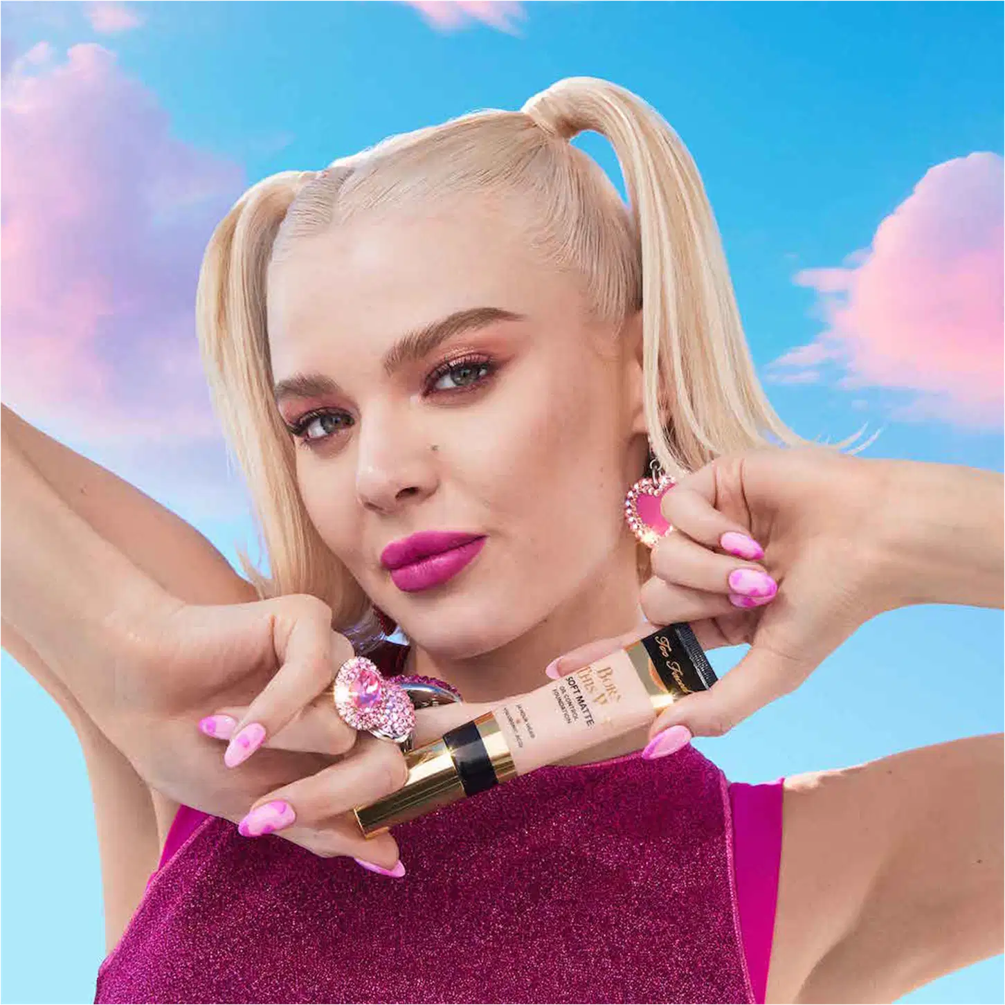 A imagem mostra uma mulher super produzida segurando uma embalagem da base próxima ao queixo.