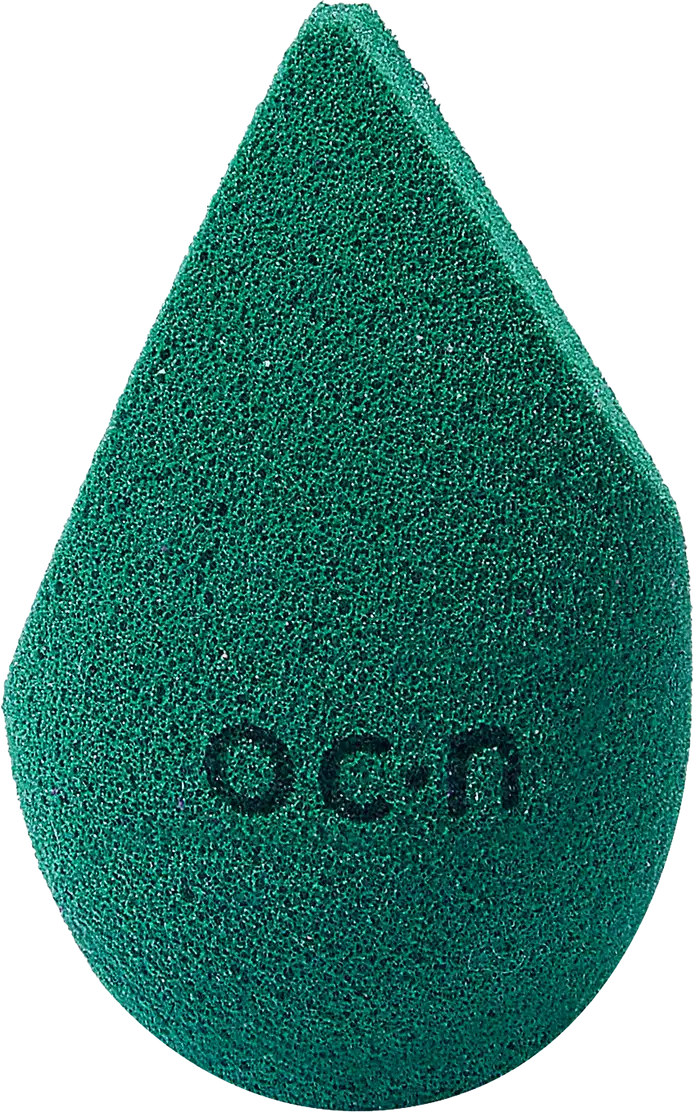 Esponja de maquiagem verde escuro com textura aveludada. Formato de gota com a palavra "Océane" impressa em relevo na superfície.