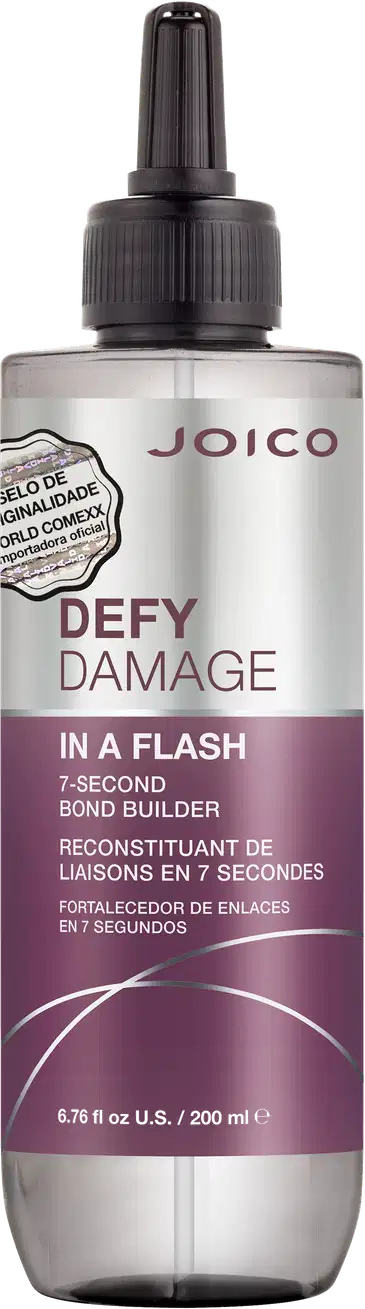 É um produto de tratamento capilar da marca Joico. A embalagem é um frasco que tem um aplicador preto na parte superior. O rótulo na frente é predominantemente branco e roxo. O nome do produto "Defy Damage In a Flash" está escrito em letras grandes;