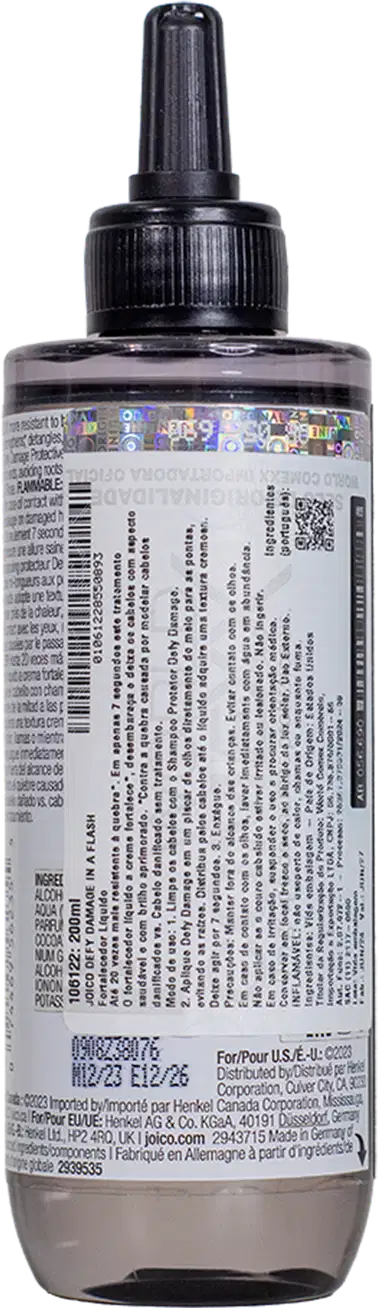 Imagem mostra o verso do produto com rótulo branco com texto informando código de barras e informações do produto visíveis no rótulo. Formato cilíndrico alongado típico de embalagens de produtos capilares líquidos.