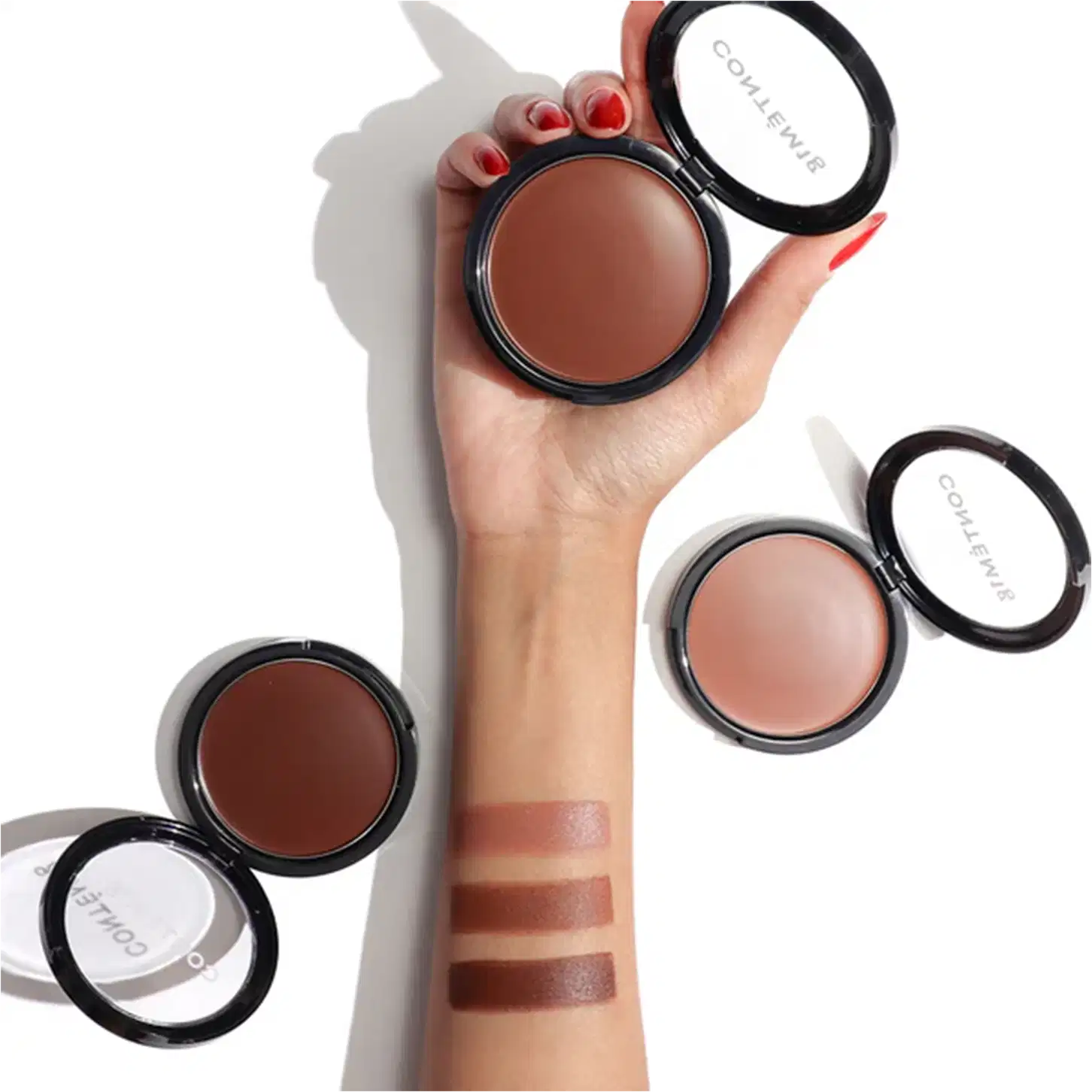 A imagem mostra um antebraço com as três opções de cores disponíveis do bronzer, além dos três produtos abertos perto do braço.