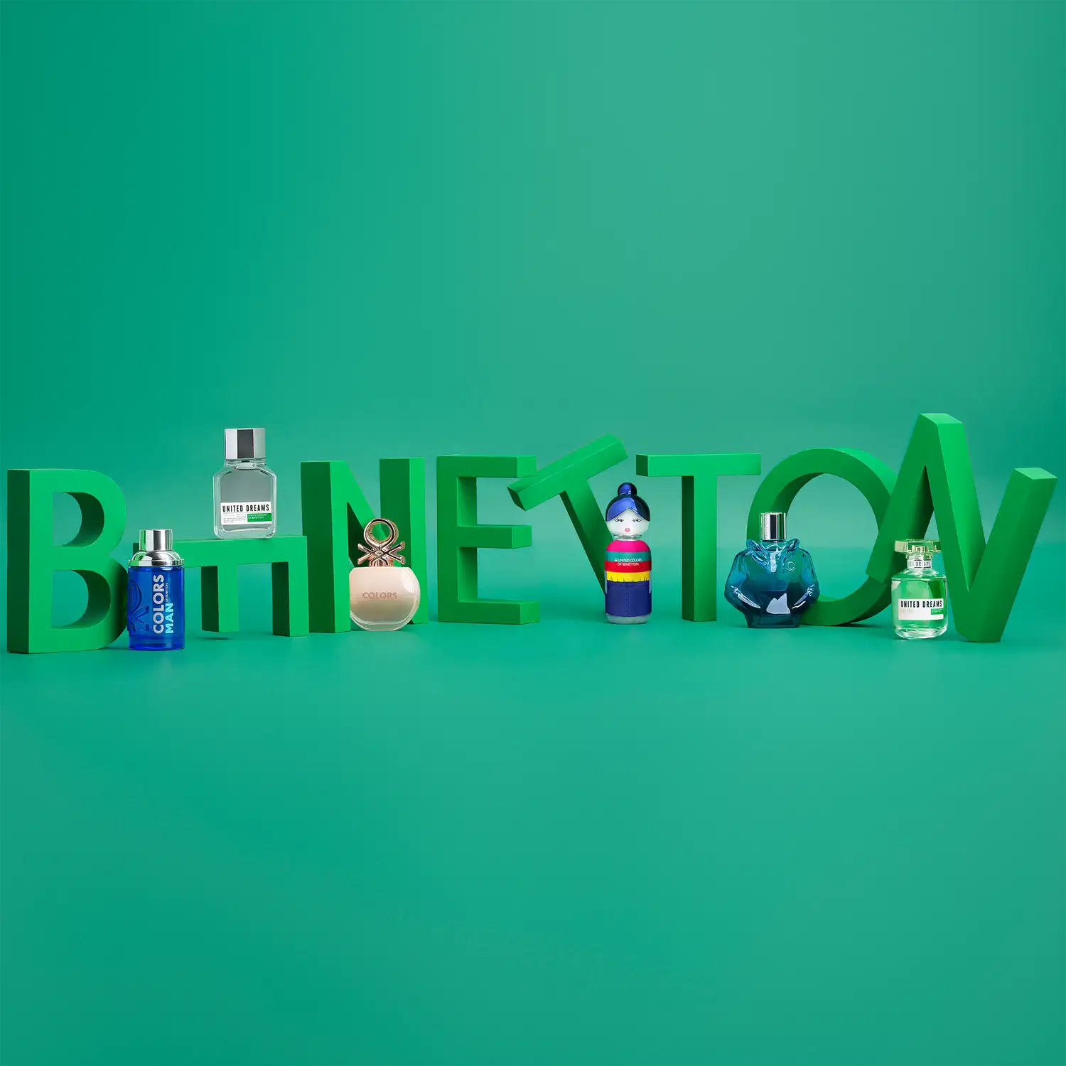 A palavra Benetton formada por letras verdes com alguns frascos de perfume da marca apoiando em cada letra.