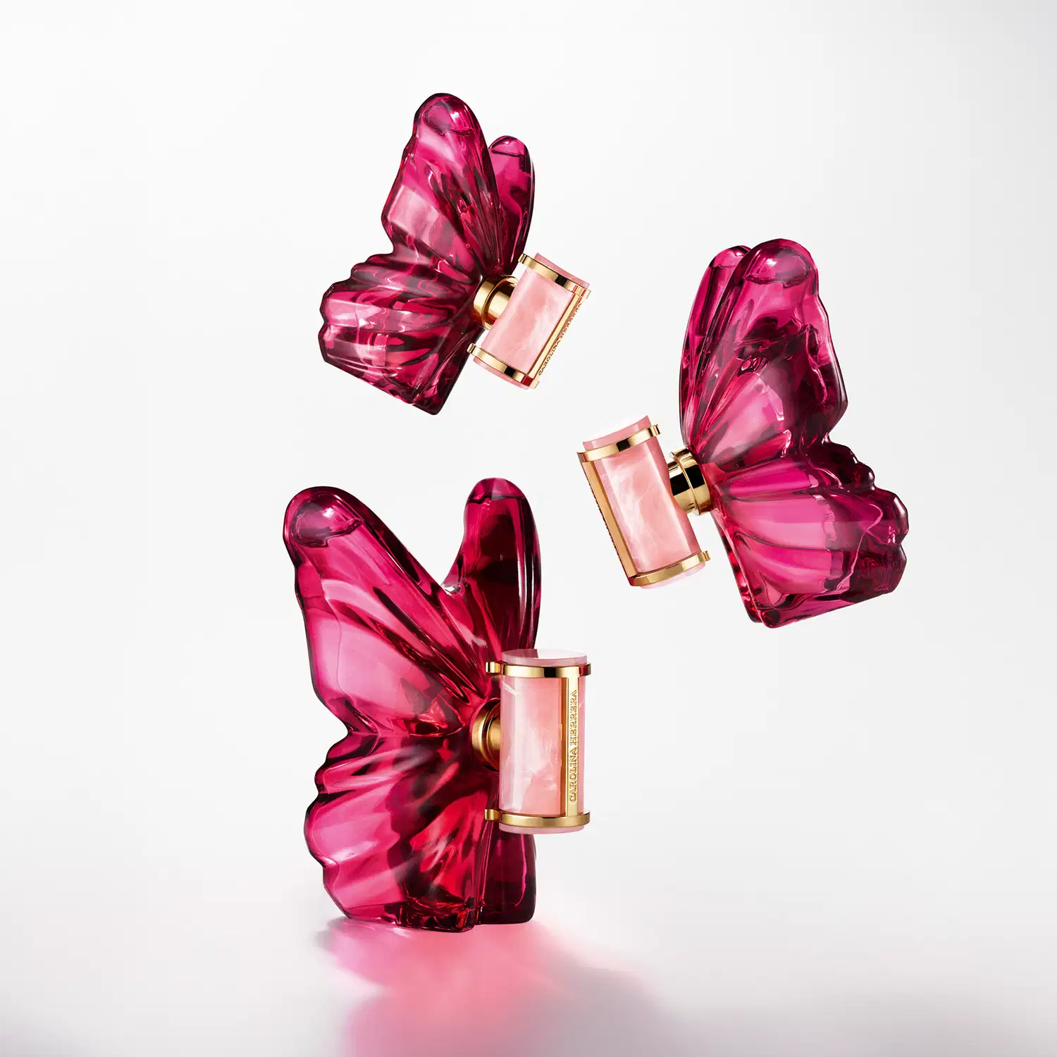 Frasco de perfume Carolina Herrera em formato escultural e vibrante na cor rosa, com rótulo dourado destacado contra fundo preto.
