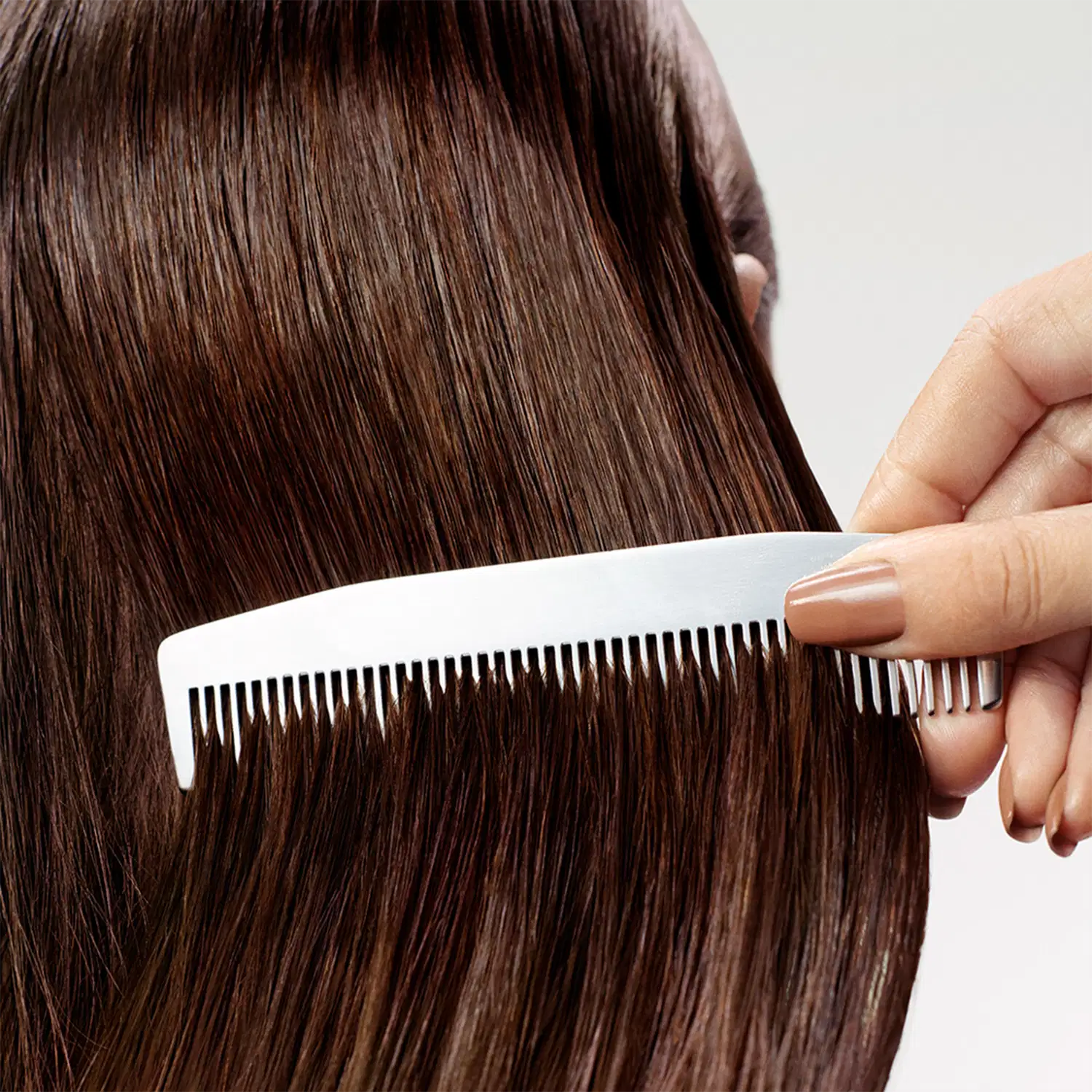 A mão de uma pessoa segura um pente de cabelo preto e branco, penteando um cabelo liso e escuro. O ambiente sugere um contexto de cuidados capilares, possivelmente em um salão de beleza ou ambiente doméstico.